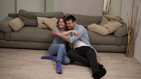 Attractive-young-couple-enjoying-leisure-together-and-embracing-while-sitting-on-the-floor-in-domestic-room.-Handsome-young-man-hugging-charming-woman-and-talking-at-home.-Loft-interior