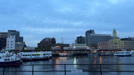 dusk view of city waterfront with boats and illuminated buildings, tranquil urban scene, wide shot