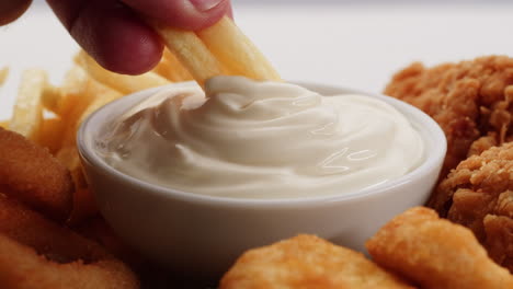 hand dipping french fries in mayonnaise sauce with other fast food items