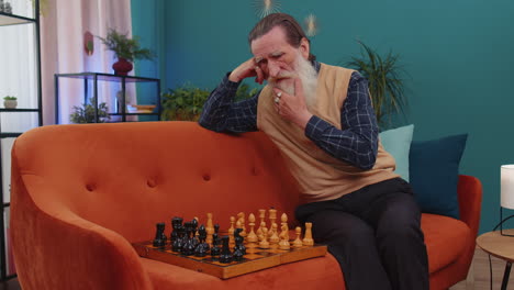 Focused-senior-grandfather-man-playing-chess-leisure-board-game-alone,-domestic-activity-at-home