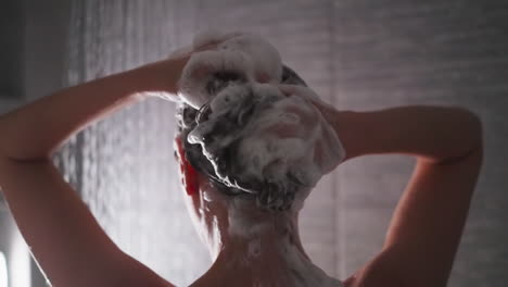 mujer masajea el cabello espumoso en la cabina de ducha de cerca. señora tranquila lava el cabello con champú durante los procedimientos de cuidado en el baño. rutina de belleza