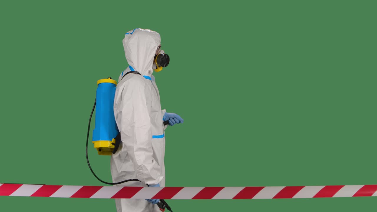 trabajador desinfectante en un traje blanco protector, respirador y gafas hace la desinfección en una pantalla verde aislada clave de croma. cámara lenta.