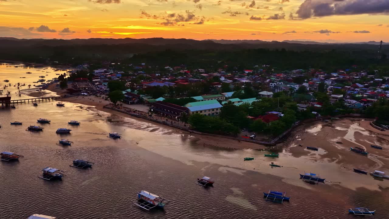 Filipinler'deki Poblacion V üzerinde renkli bir gün batımı gökyüzünü boyarken tekneler sakin sularda dinleniyor