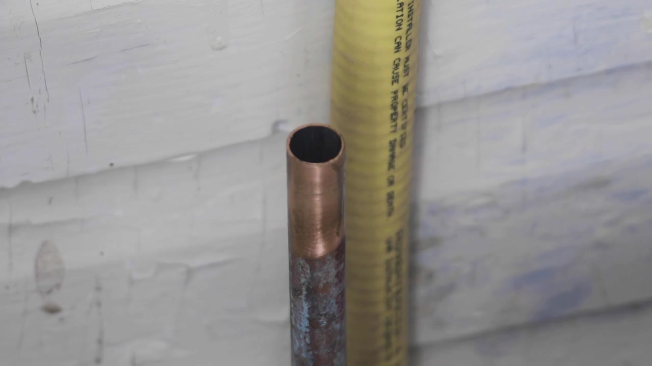 A man uses sandpaper on an old copper pipe before soldering. Right pan, closeup.