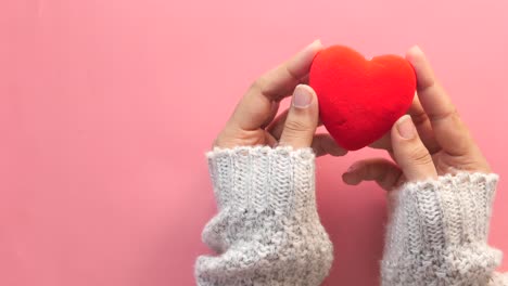 en manos con guantes tejidos sosteniendo un corazón rojo