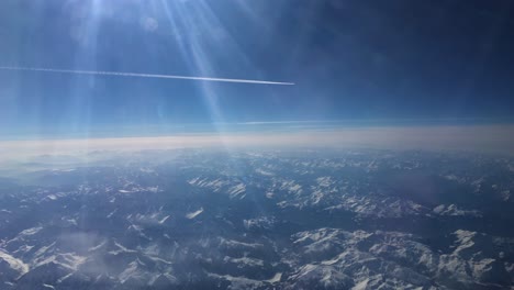 footage from an airplane showing an airplane white trail flying far away and snowy mountains from above the alps in europe 2