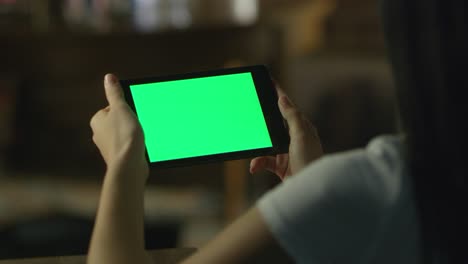 una adolescente está usando una tableta con pantalla verde en modo retrato por la noche. estilo de vida casual.