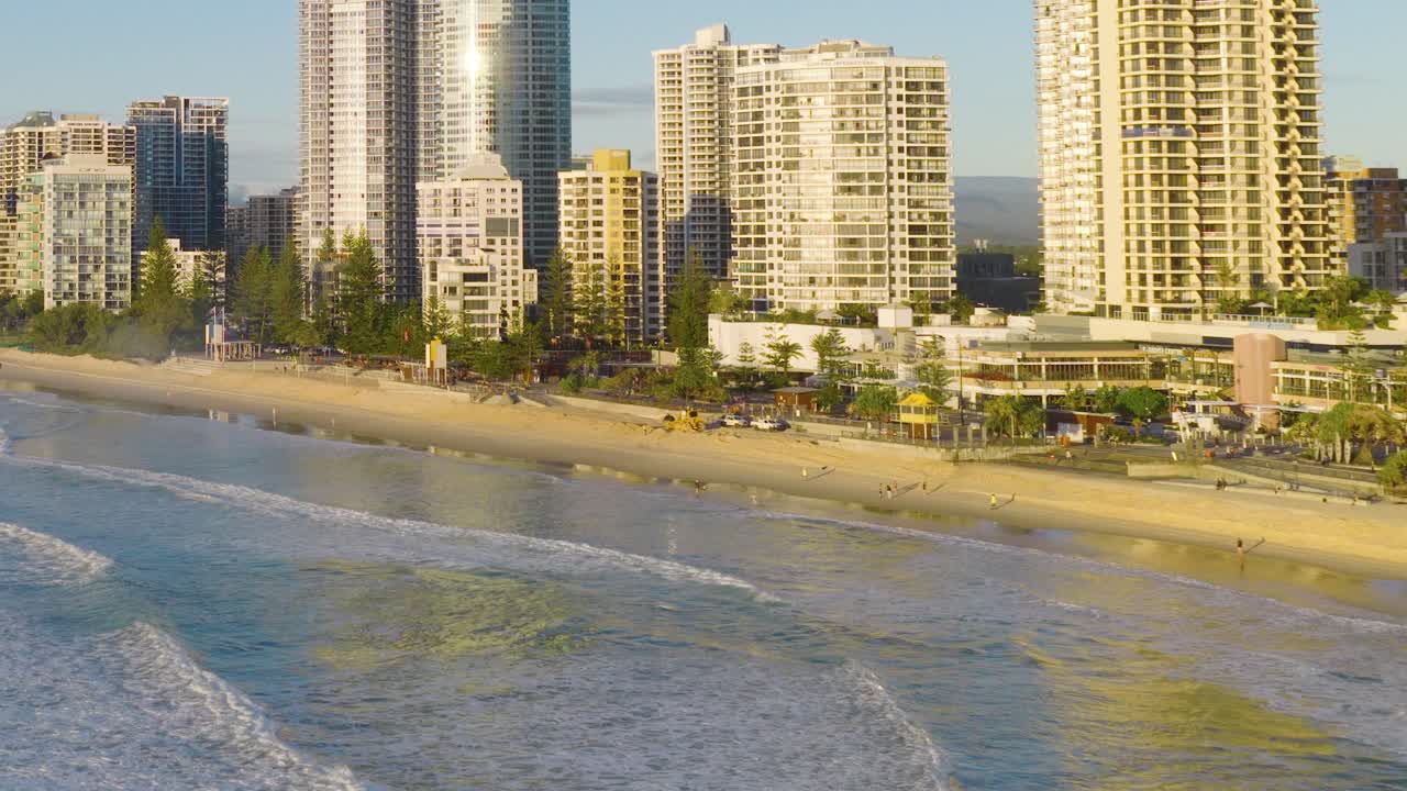 Aerial footage captures Gold Coast's beachfront skyline with high-rise buildings, sandy shores, and gentle ocean waves under warm sunlight