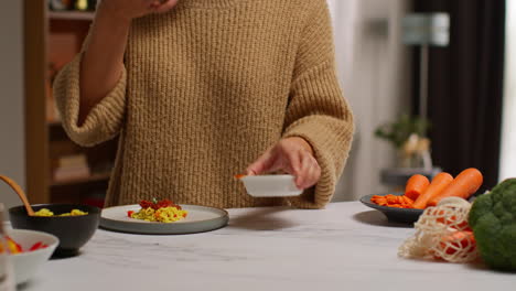 close up of woman at home in kitchen preparing healthy vegetarian or vegan meal pouring sauce onto orzo pasta and roasted tomatoes