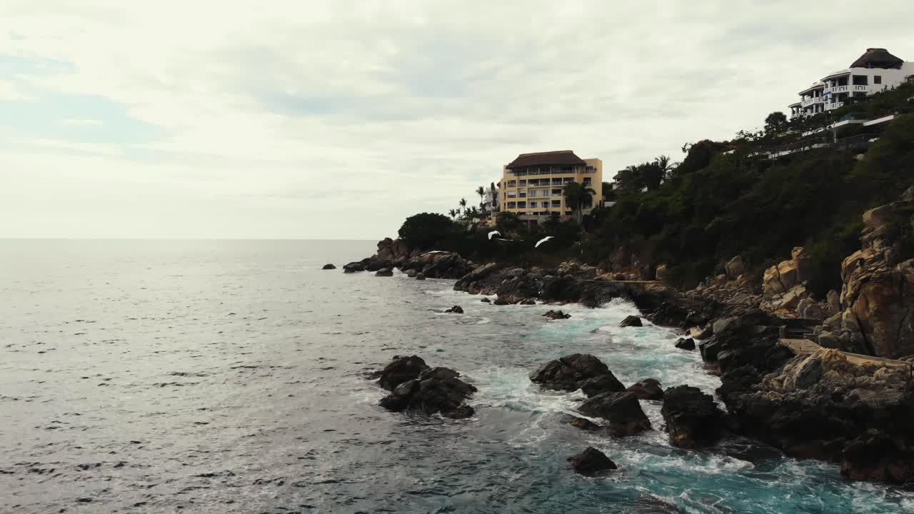 Puerto Escondido's rocky coastline with villas and flying seagulls