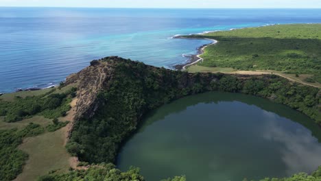 aerial view of volcanic crater lake with green water surrounded by cliff and greenery, overlooking blue ocean, comoros islands