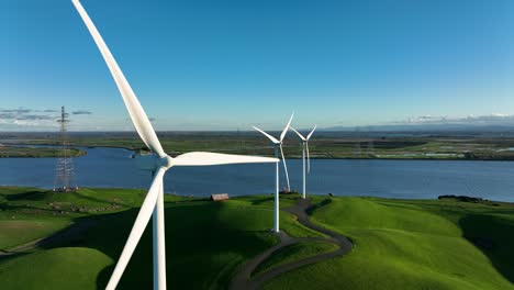 Wind-Turbines-spinning-in-Slow-Motion-along-river-and-green-hills,-Montezuma-Hills,-Northern-California