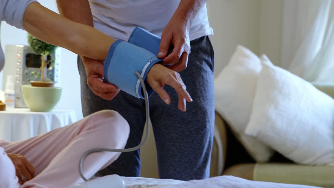 Front view of mature caucasian man measuring blood pressure of caucasian woman at home 4k