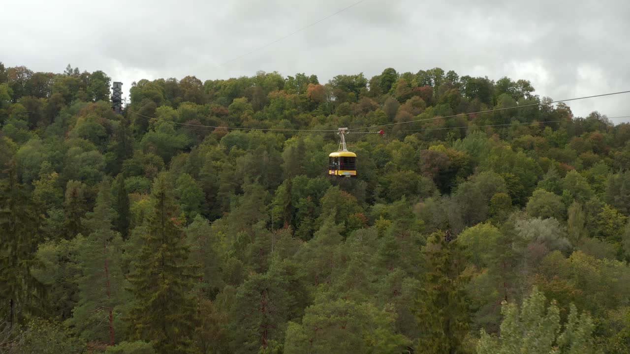 Cable car over green lush forest park in autumn. Close up of a yellow tourist cable park. 4k footage.