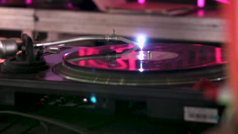 close shot of a the turntable of a dj moving in slow motion in a party with pink lights