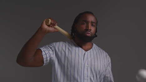 studio portrait of serious male baseball player wearing team shirt holding bat and throwing ball in the air shot against grey background 2