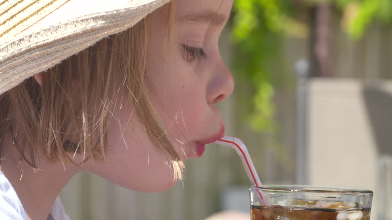 An adorable young girl taking a refreshing sip of cola outside on a hot summer day