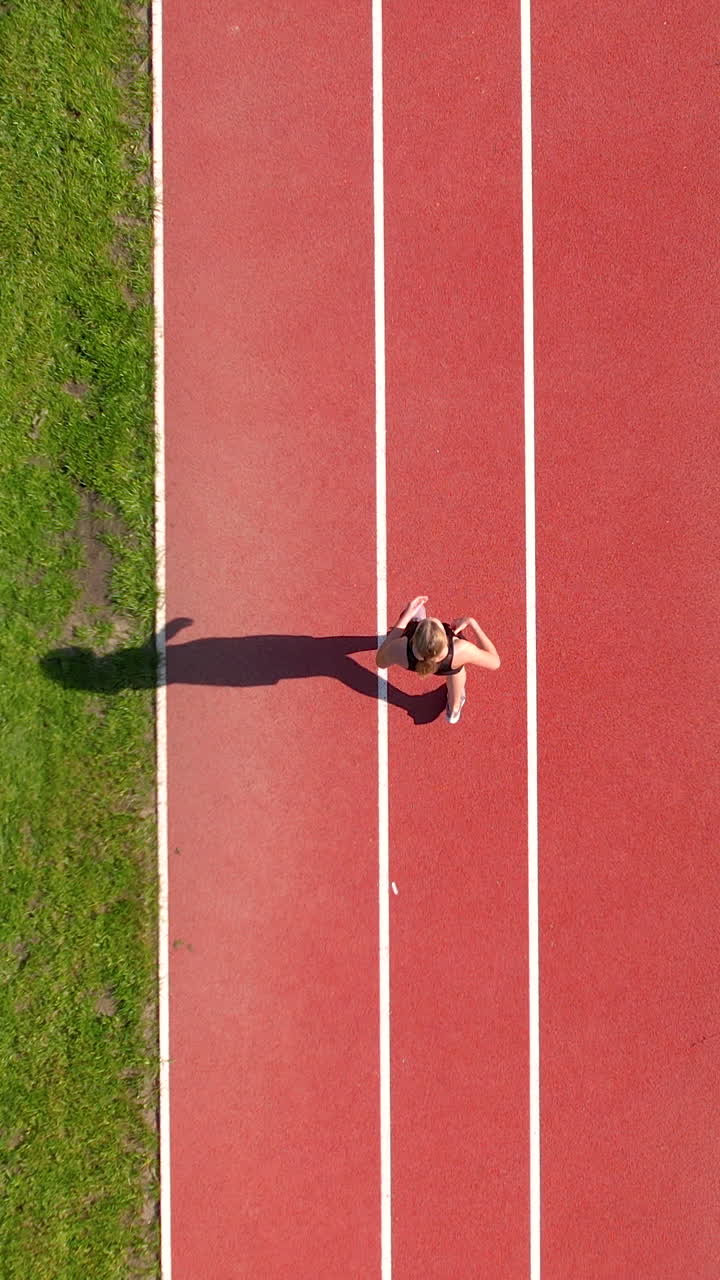 Birds eye view of a female athlete sprinting on a red running track during a sunny day. Ideal for fitness, sports training, and healthy lifestyle content