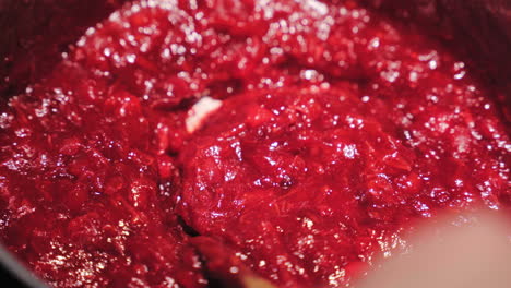 Mixing-cranberry-sauce-with-wooden-spoon,-close-up-view