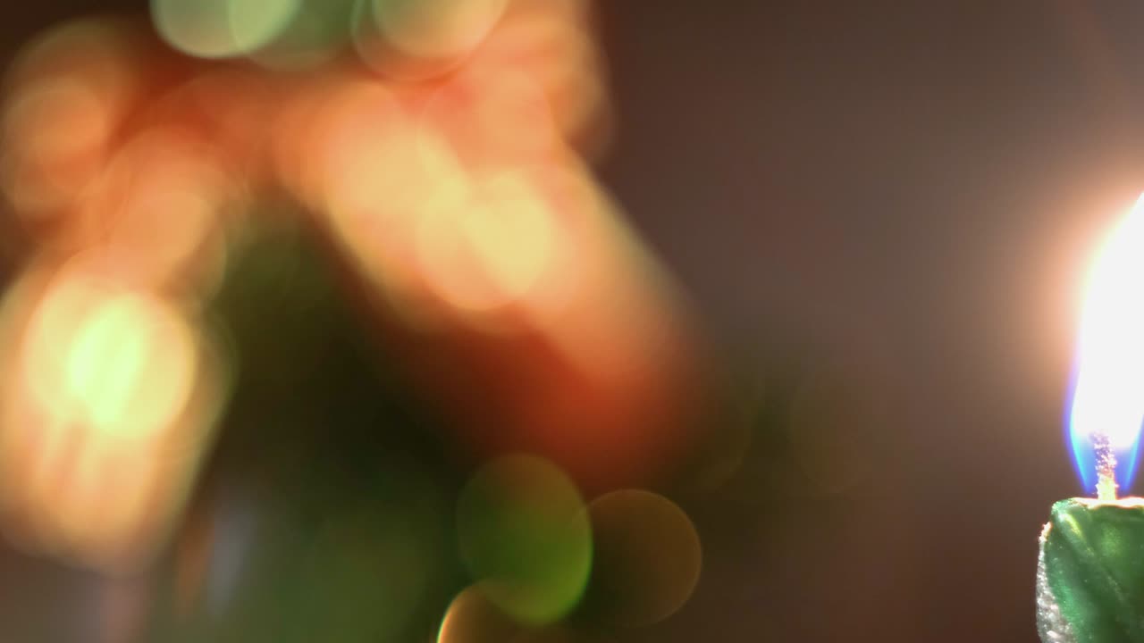 una vela verde ardiente contra un árbol de navidad borroso