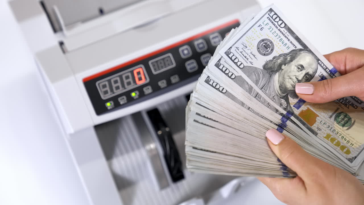 Bundle of one hundred dollar banknotes. Female's hands holding a large sum of money of dollar bills on the background of automatic counting machine.