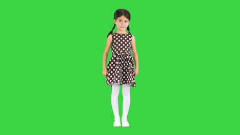 little girl in polka dot dress standing and putting hands to her head on a green screen, chroma key