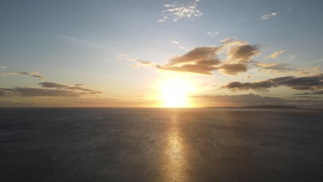Breathtaking ocean sunset in the Philippines, with golden hues reflecting on the calm sea, scattered clouds, and a distant island on the horizon.