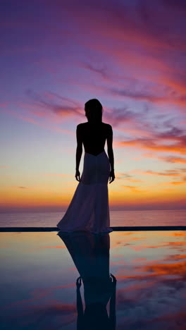 woman in white dress silhouetted against a vibrant sunset with reflection