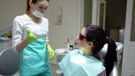 Young-woman-in-red-protective-glasses-rinsing-her-mouth-with-treatment-at-the-dentist.-Glass-with-green-fluid-in-her-hand.-Shot-in-4k