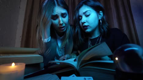 dos mujeres leyendo cartas de tarot y libros en la noche