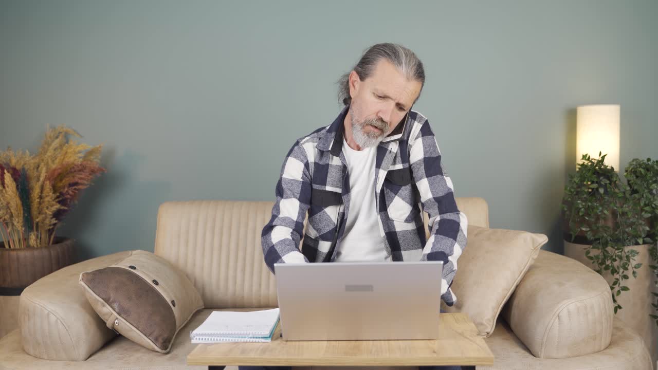 hombre usando una computadora portátil hablando nerviosamente por teléfono.