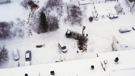 maintenance workers replacing electricity pole on snowy rural village by the apartment building, aerial view