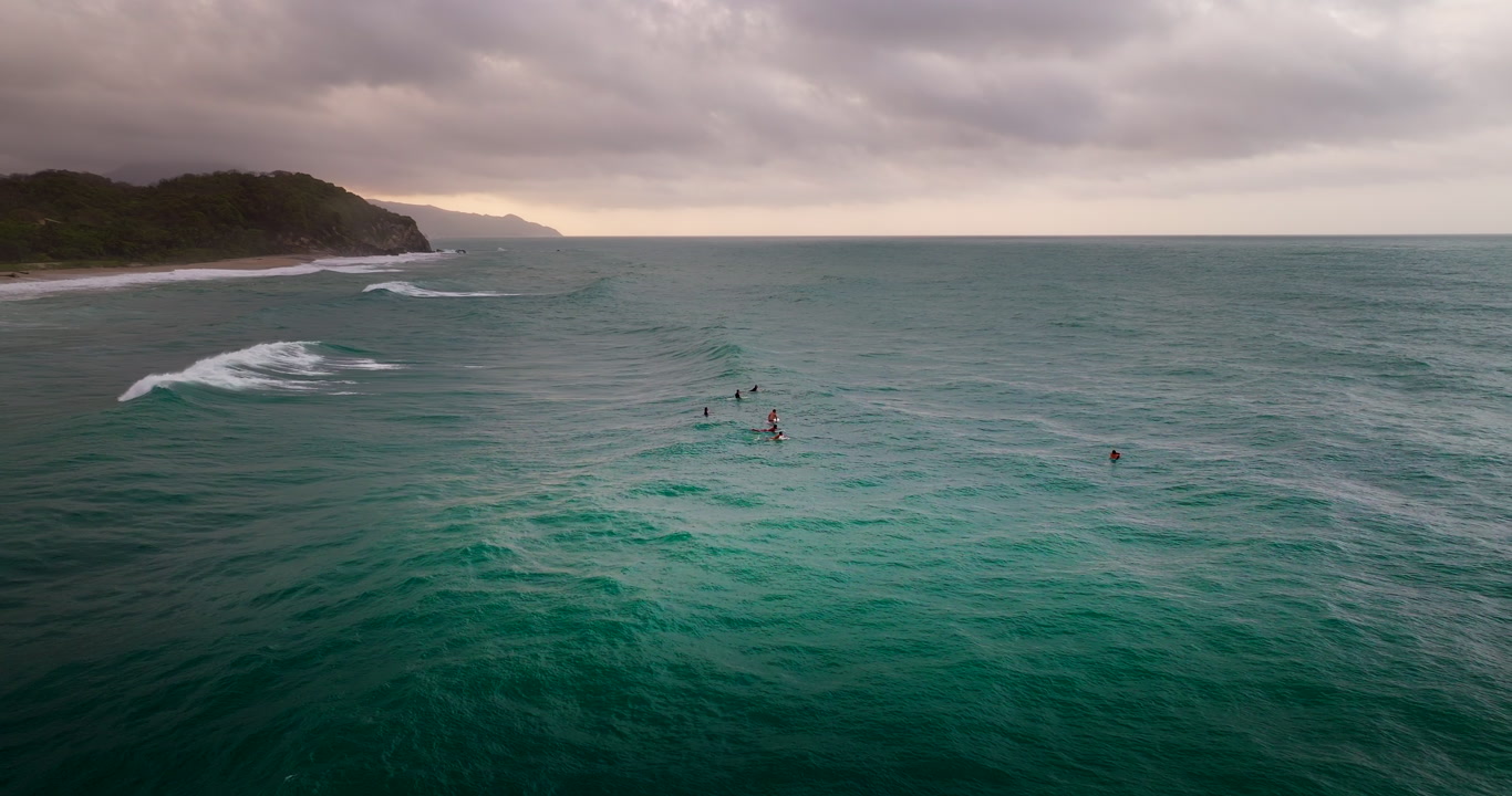 Group of surfers waiting for waves in the turquoise water of Los Naranjos beach near Tayrona Park, Colombia. Aerial drone, copy space