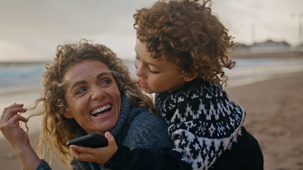 Mom son having fun on ocean shore closeup. Adorable kid hug mother talking phone