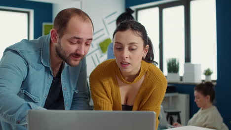 Colleagues-in-startup-office-talking-about-marketing-strategy-looking-at-laptop-screen