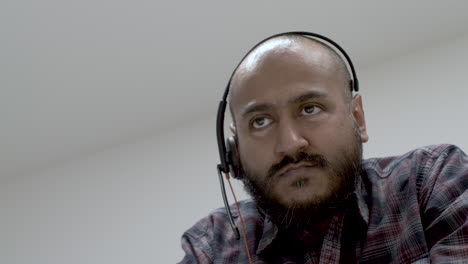 a bald bearded male wearing a headphone speaking with someone being in a light room