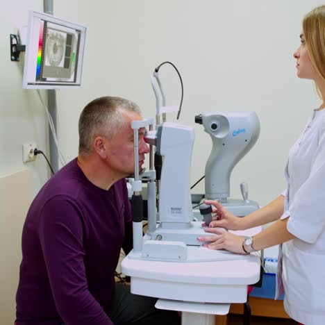 mature man checking his eyes in clinic. young optometrist testing patient's eyes on a special machine. specialist looking at the screen of a monitor.