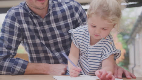 father at home at kitchen counter helping young daughter to draw picture in book - shot in slow motion