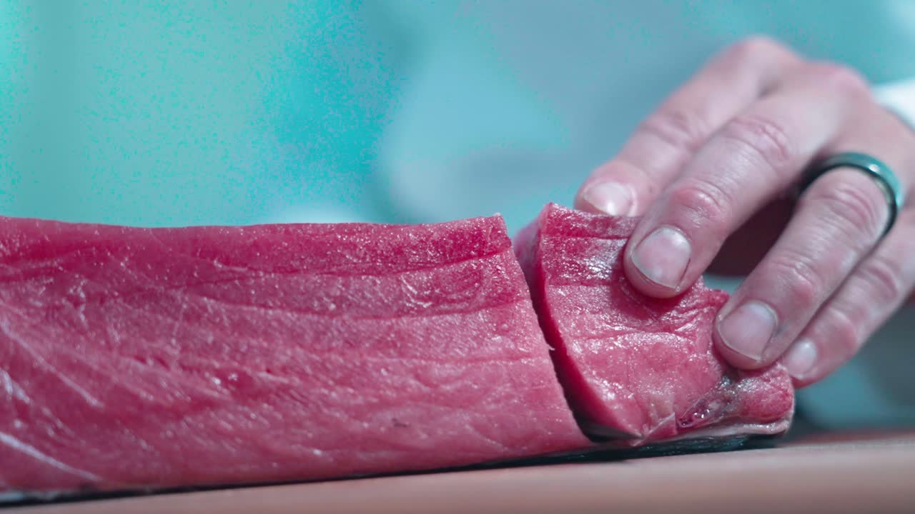 A static close-up shot captures a slab of tuna receiving its first precise cuts, highlighting the texture and freshness. Ideal for culinary, sushi preparation, and professional kitchen content.