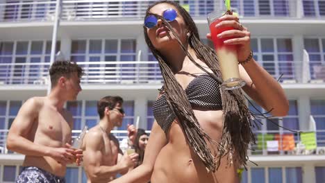 young beautiful girl with dreads and sunglasses coming closer to camera while dancing on the pool party. happy friends in