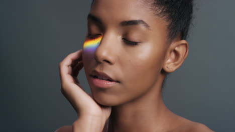 retrato multicolor hermosa mujer afroamericana tocando la cara acariciando la piel suave disfrutando del cuidado de la piel belleza con luz colorida que se refleja en la tez suave