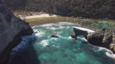 Vista-Aérea-De-La-Playa-De-Atuh-En-Nusa-Penida,-Indonesia-En-Un-Día-Soleado-Y-Con-Agua-Azul-Cristalina-Golpeando-Las-Formaciones-Rocosas