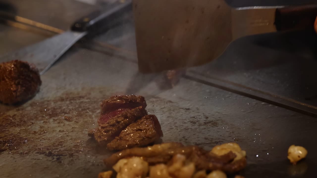 Primo piano di uno chef che affetta bistecca e funghi su una griglia calda con una spatola