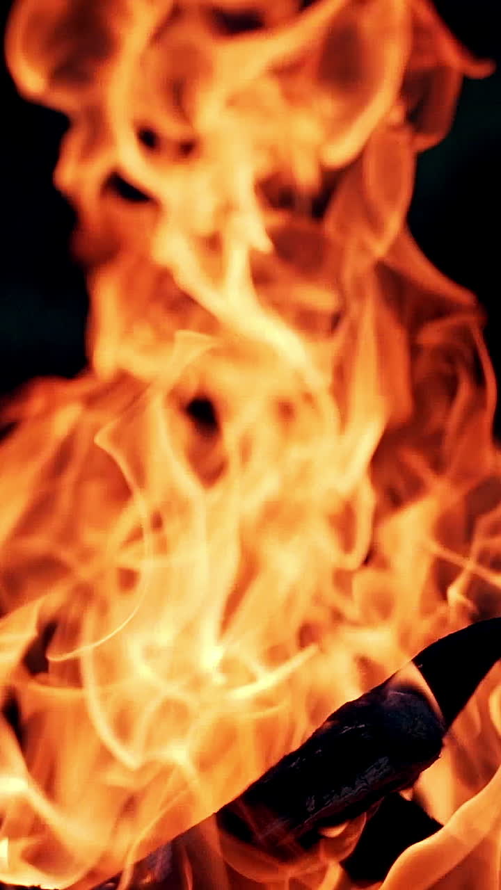 Bright flame from smoldered logs on dark background. Wood burning slowly with orange fire flame. Close-up. Vertical video