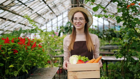 woman in greenhouse holding a wooden crate of fresh vegetables