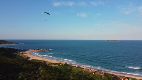 paraglider flying over mountains on coast of atlantic ocean aerial tracking shot