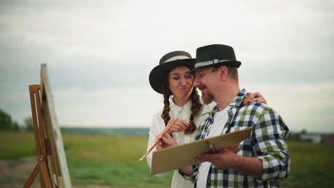 a heartwarming scene of a couple outdoors, both wearing hats. the man, dressed in a checkered shirt, is holding a palette while the woman playfully touches his face with a piece of grass