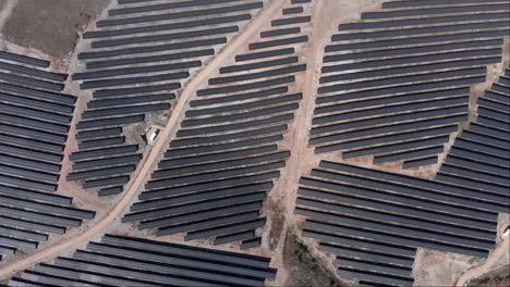 ascending-Drone-top-down-view-over-photovoltaic-solar-power-park-row-panels-hills-sunny