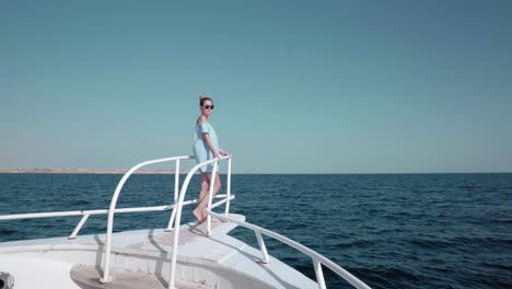 portrait of a young beautiful sexy caucasian woman on a yacht in in a blue dress and sunglasses. the concept of vacation, freedom, sunny summer. blue ocean on backgroung. far view