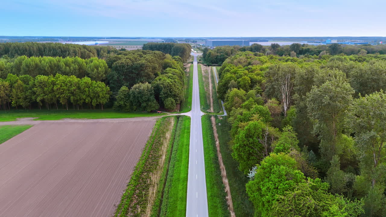 Straight highway along the fields and forest. Drone footage above the road. Storehouses at backdrop.
